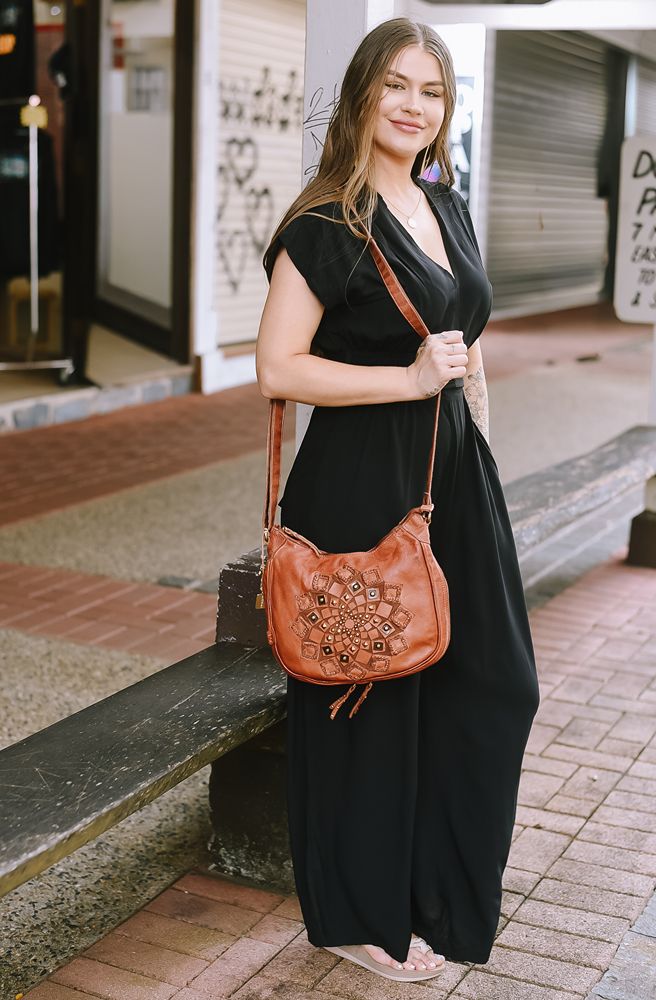 Woman in a black dress holding a brown leather handbag on a city street.
