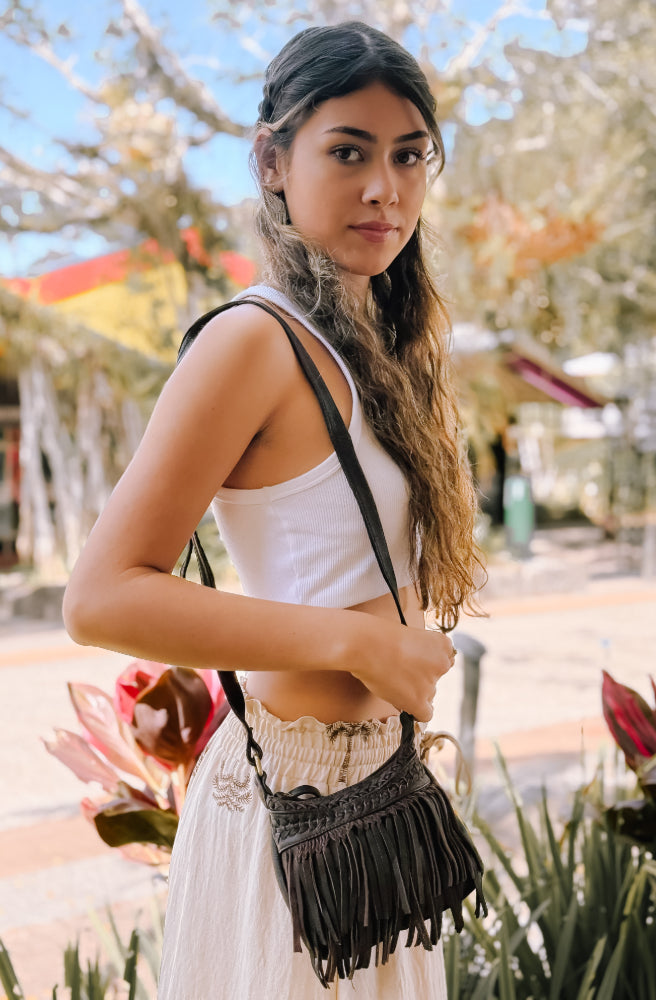 Baby Nayeli Bag, Woman wearing a white top and white skirt with a dark brown fringed leather bag outdoors.
