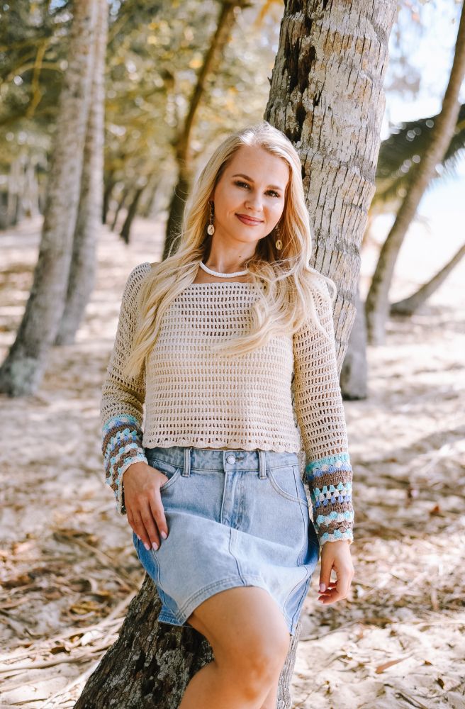 Woman standing in a forest wearing a patterned sweater and denim shorts.
