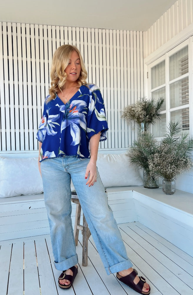 Jaase Asteria Print Gabriella Top, Woman wearing a blue floral blouse and jeans standing on the white verandah.