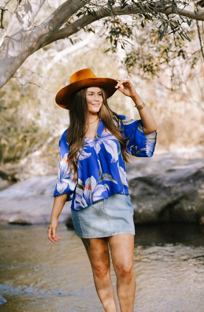 Woman wearing a blue floral kimono and brown hat by a stream