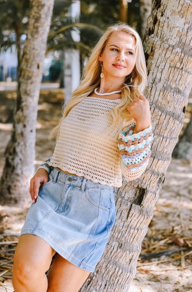 Woman in a crochet top and denim skirt leaning against a tree in a natural setting