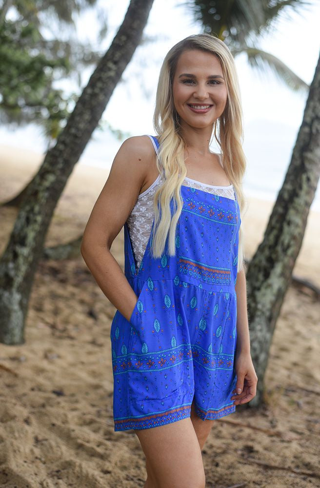 Woman wearing a blue short overalls with a pattern, standing in a natural setting with trees.