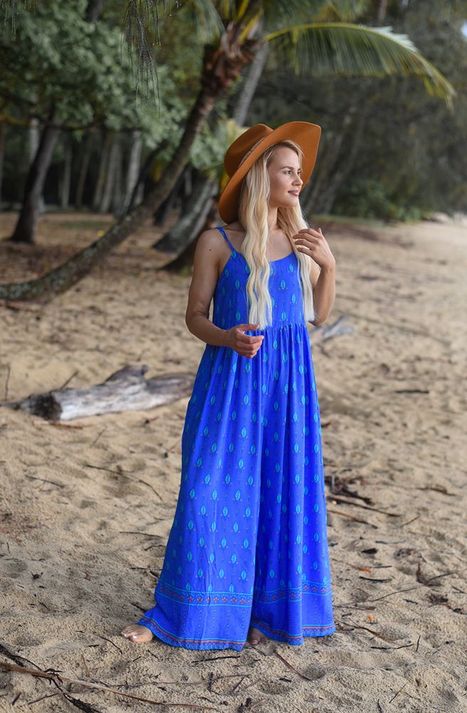 Woman in a blue pantsuitand hat standing on a sandy beach with palm trees in the background
