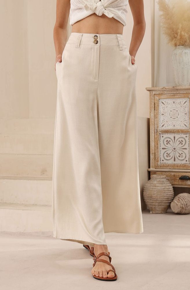 Woman wearing beige wide-leg pants with a white top in a neutral setting.