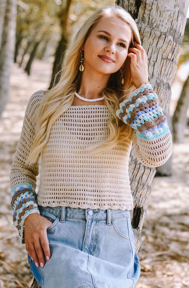 Woman wearing a crochet sweater with colorful sleeves in a natural setting
