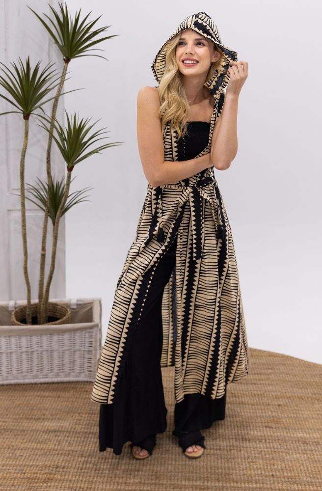 Woman wearing a long, patterned kimono with a hood in a room with plants and a basket.