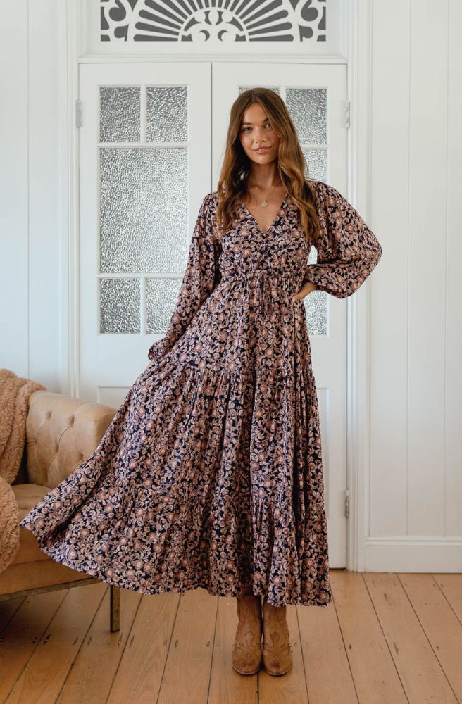 Woman wearing a floral dress standing in a room with wooden floor and decorative wall.