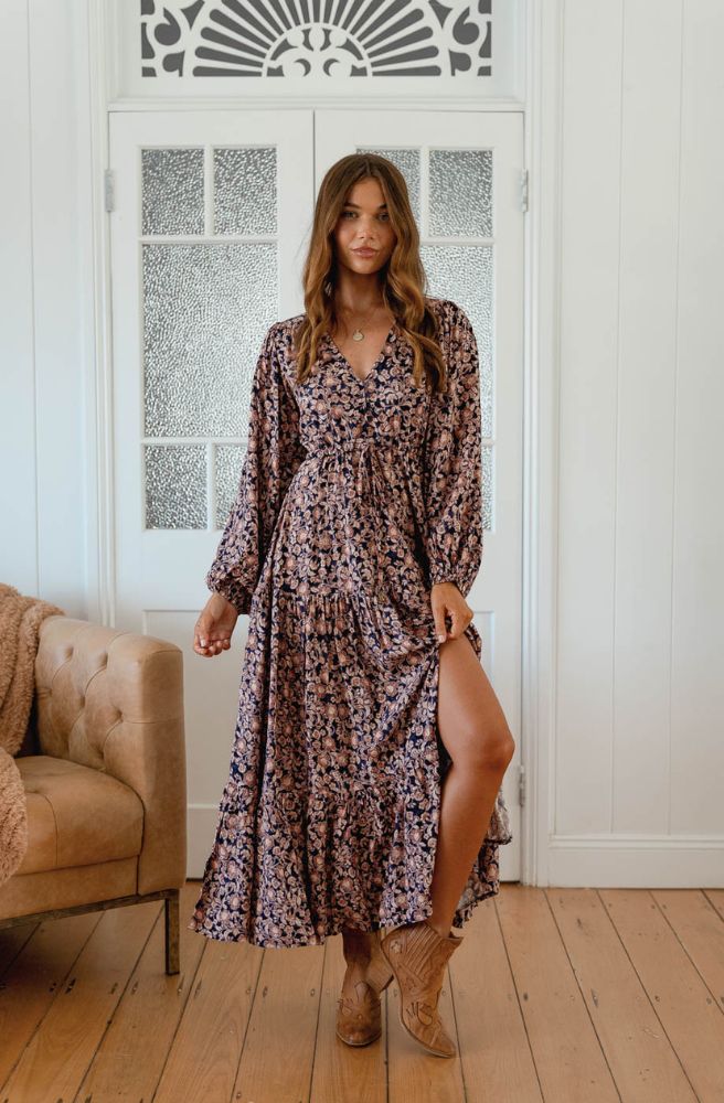 Woman in a floral dress standing in a room with wooden flooring and a decorative wall.