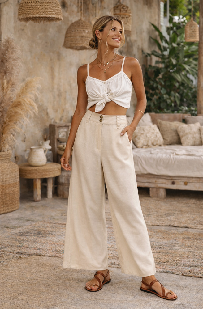 Woman in a white top and beige pants standing in a rustic outdoor setting.