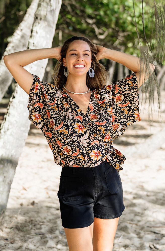 Woman wearing a floral blouse and black shorts standing in a natural setting with trees.
