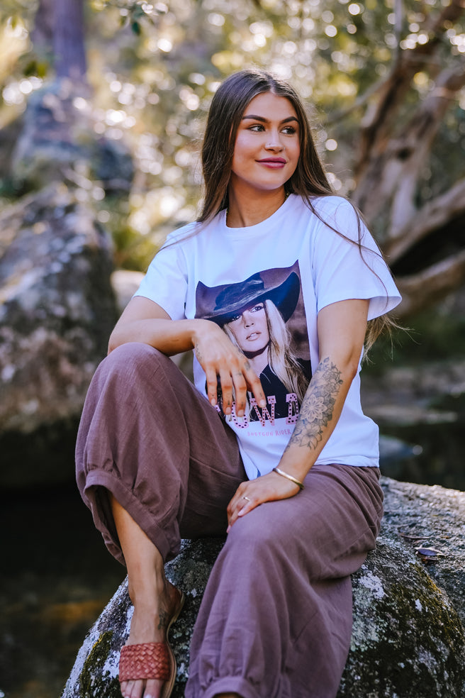 Woman sitting on a rock wearing a white t-shirt with a graphic design.