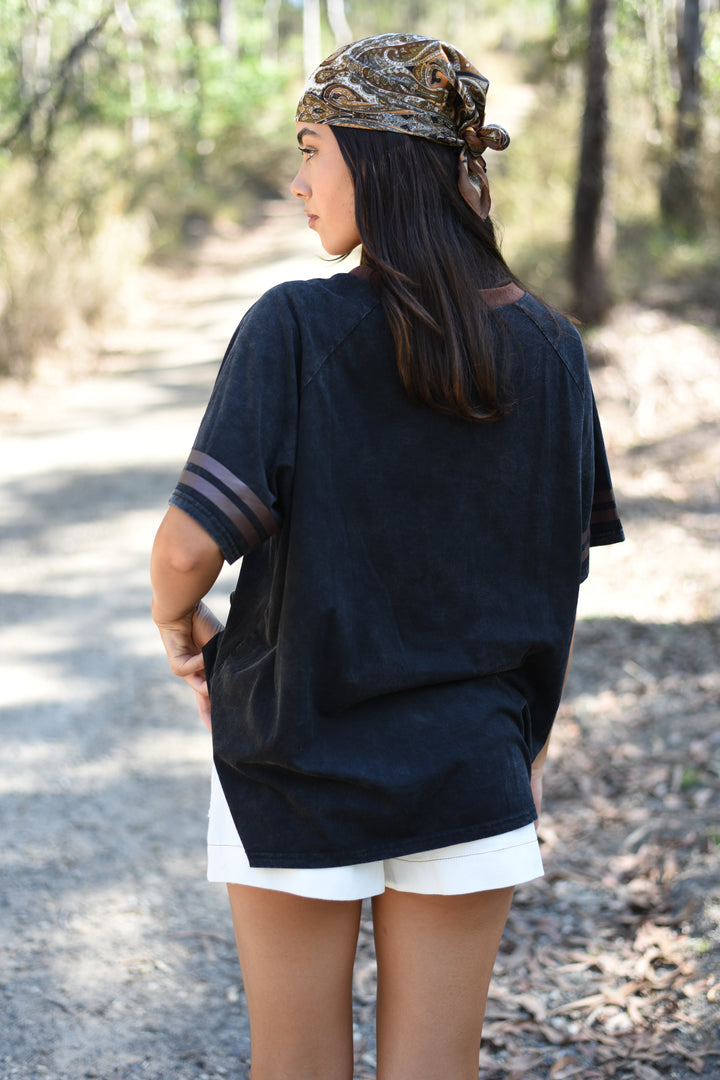 Back view of the Black Love of Vino Tee showing its washed black fabric, relaxed fit and brown striped sleeve details.