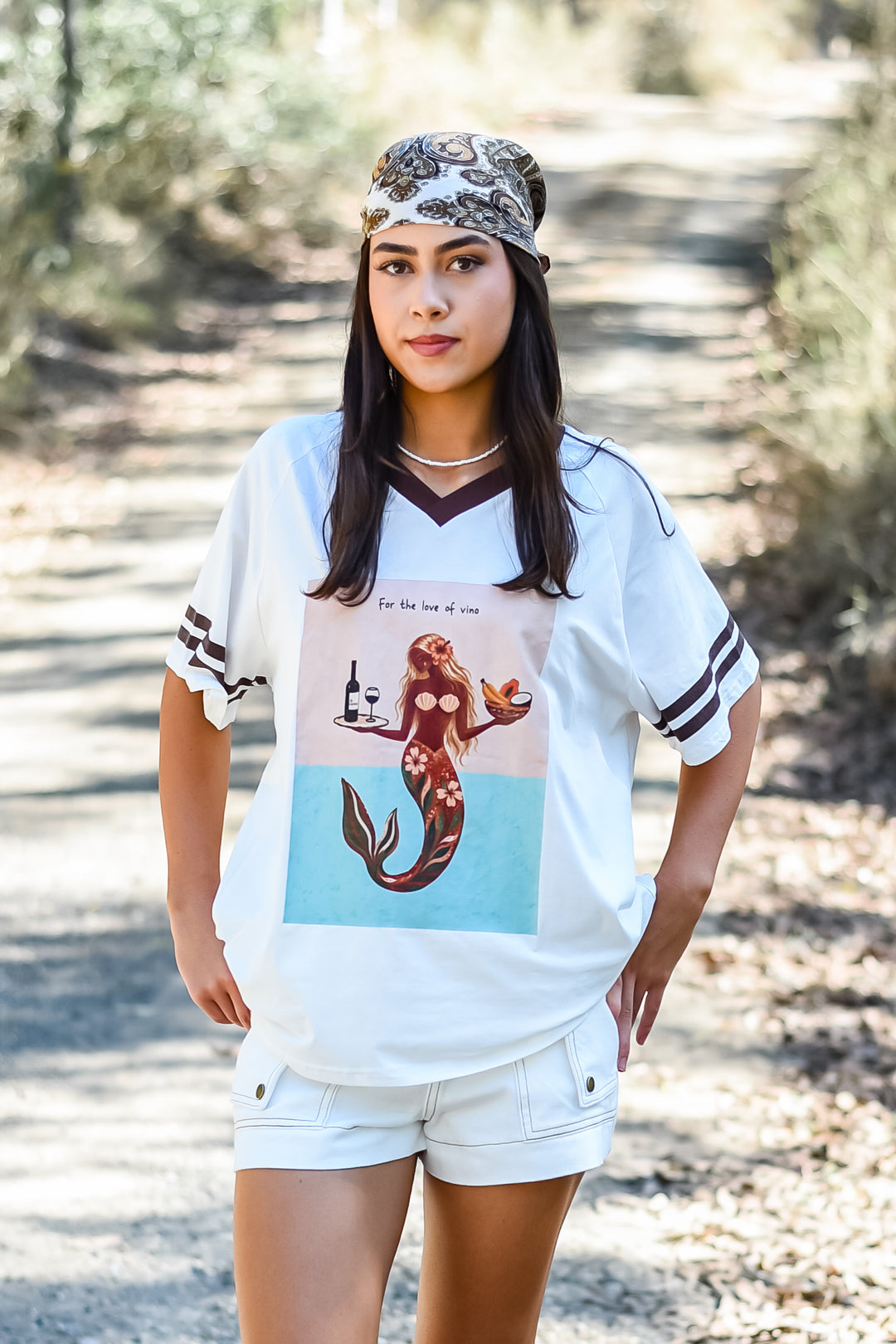 Front detail of the Choco Love of Vino Tee showing a mermaid graphic with wine and tropical fruit on a white shirt with chocolate-brown V-neck and sleeve trim.