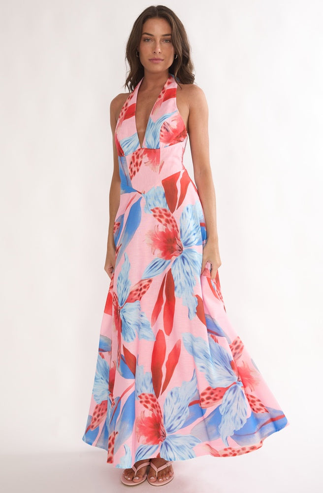 Model wearing Tonketti Coral Tropics halter maxi dress with coral and blue tropical floral print and flowing skirt.