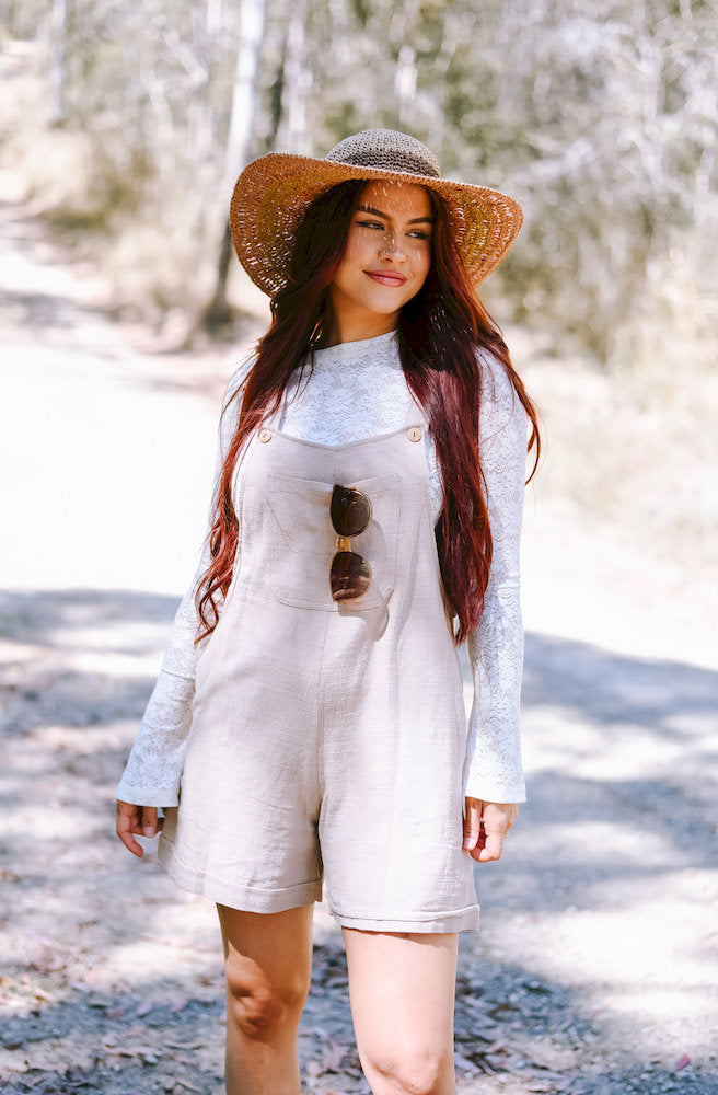 Women's cream short overalls styled with a white lace blouse, featuring a relaxed fit, adjustable straps and practical pockets
