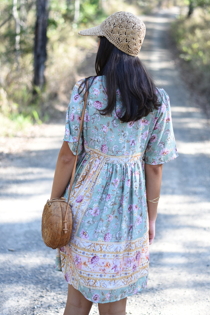 Back view of the Pastel Mosaic Mini Dress showing its floral border print and gathered babydoll silhouette.