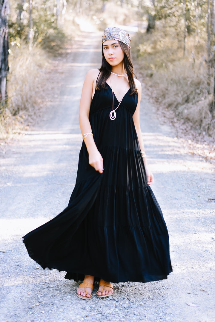 Ebony Umbrella Dress featuring a classic black maxi silhouette, a deep V neckline and a voluminous flowing tiered skirt.