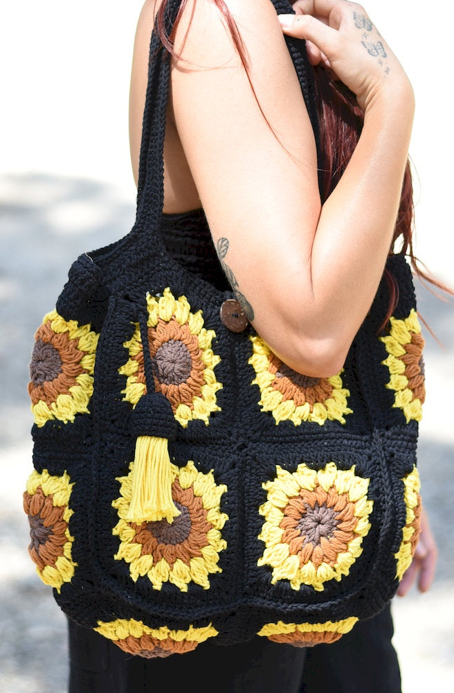 Black handmade-style crochet shoulder bag with sunflower motifs, yellow tassel and button closure styled with a relaxed bohemian outfit