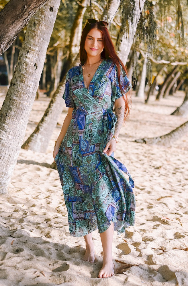 Forest Patch Mirage Wrap Dress featuring a blue, sage and turquoise paisley patchwork print, flattering wrap silhouette, flutter sleeves and flowing skirt.
