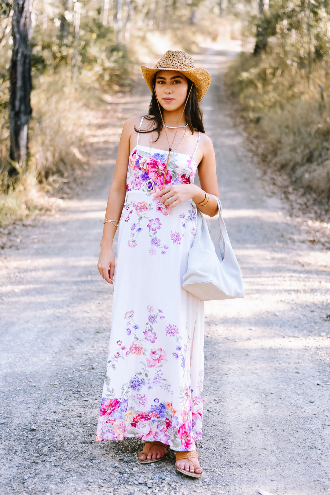 Garden Bloom Maxi Dress featuring colourful pink and purple florals on a white base, styled with a straw cowboy hat and sandals.