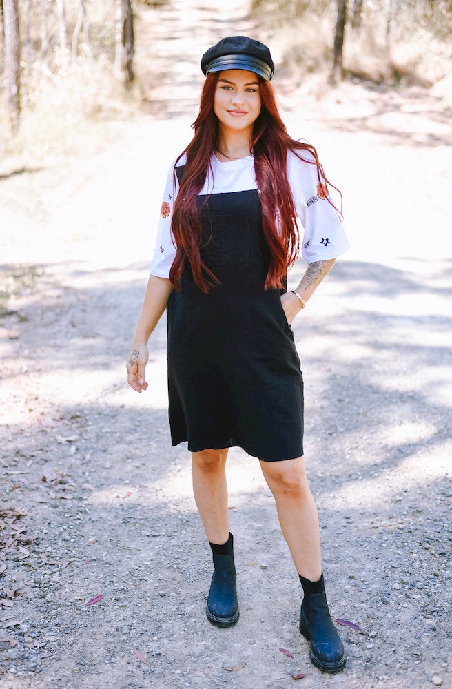 Gypsy Thread Pinafore Mid Short Black featuring adjustable shoulder straps, a front bib pocket and a relaxed knee-length silhouette.