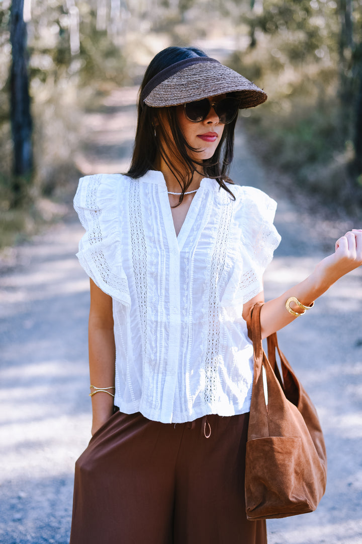 Honey wearing the Natural Choco Straw Hat with a brown band, styled with a Ivory Lace Ruffle Top and relaxed brown trousers for a casual boho look