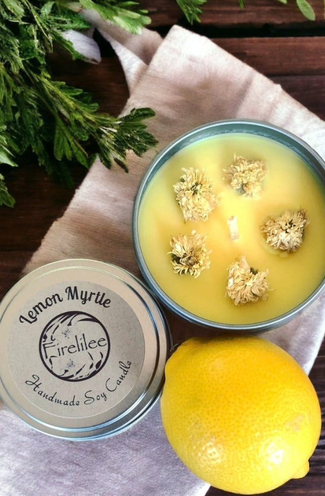 Lemon Myrtle Soy Candle in a silver travel tin with fresh lemon and botanical flowers.