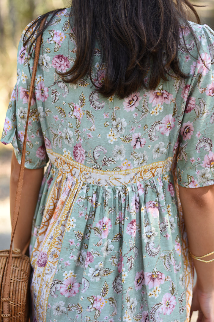 Back view of the Pastel Mosaic Lace Mini Dress showing its sage floral print, decorative border details and gathered mini skirt.
