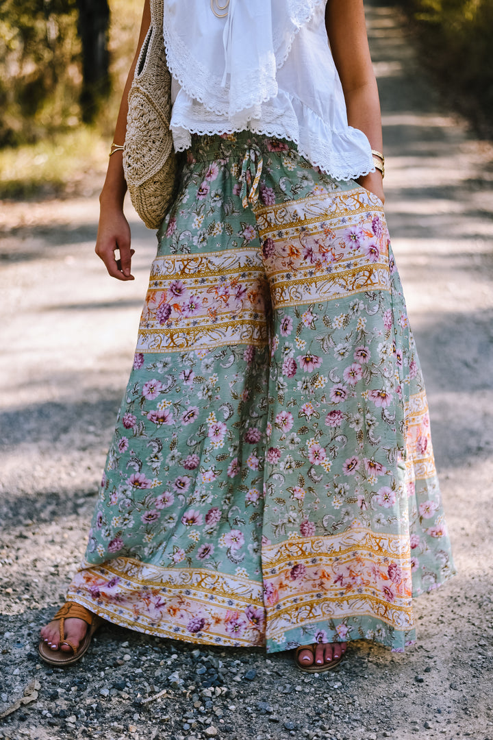 Full-length view of the Pastel Mosaic Maxi Pants styled with a white sleeveless top and sandals, showcasing the floral print and flowing legs.