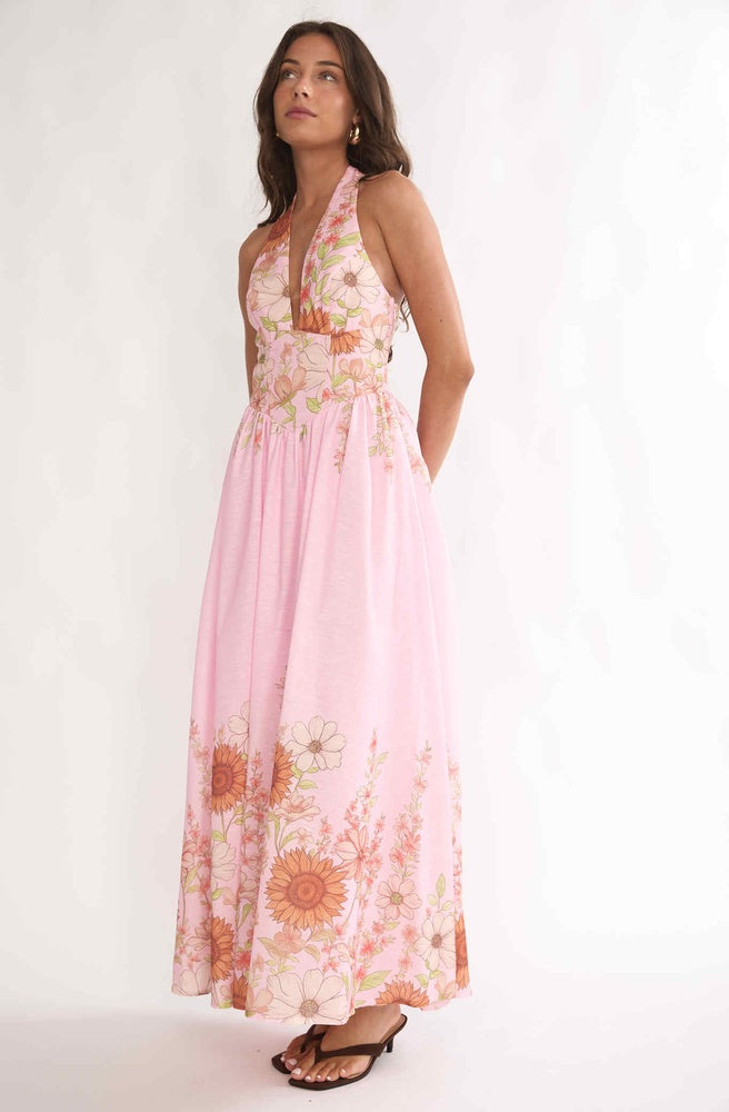 Model wearing Tonketti Pink Petal halter maxi dress with soft pink floral border print and flowing skirt.