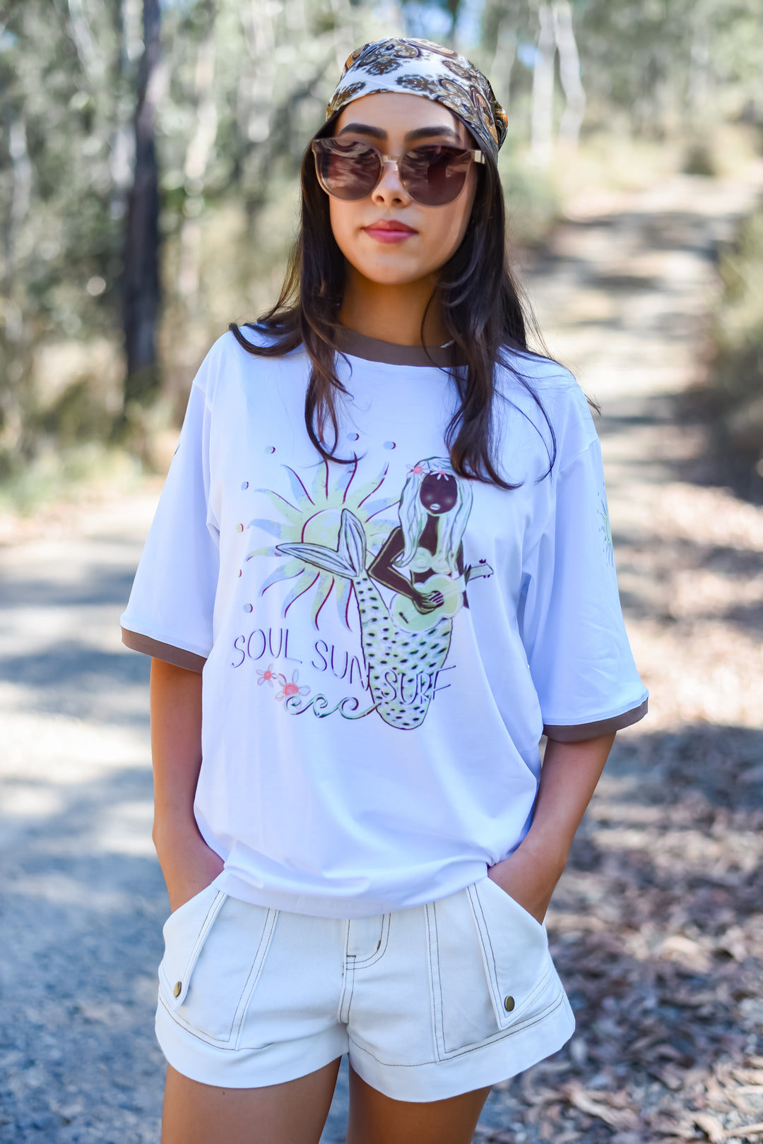 Front view of the White Soul Surf Tee featuring a mermaid playing guitar graphic with Soul Sun Surf lettering and contrasting brown trim.